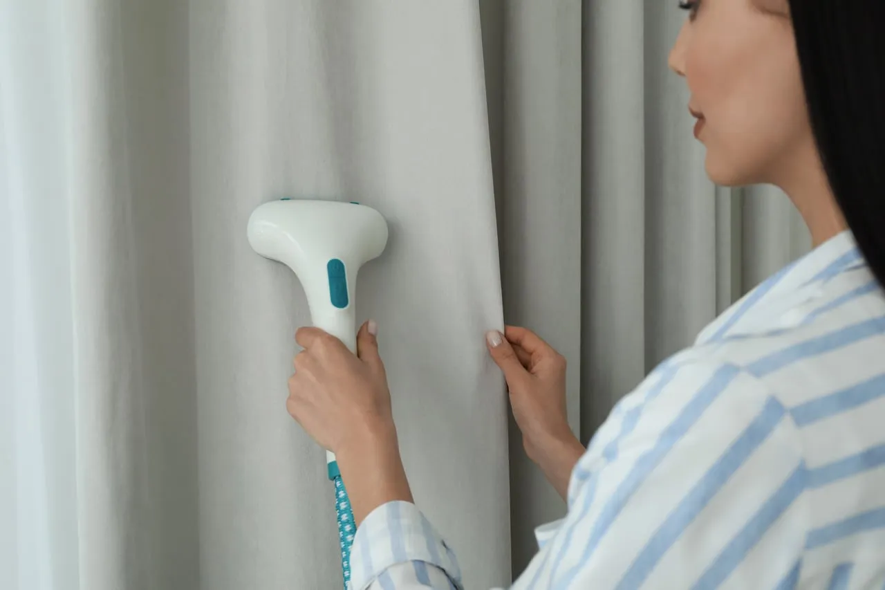 Kobieta prasująca firany parownicą, uśmiechnięta