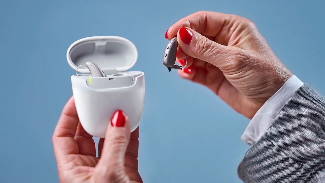 Kobieta z czerwonymi paznokciami trzyma aparat słuchowy, pokazując, jak wyregulować aparat słuchowy.