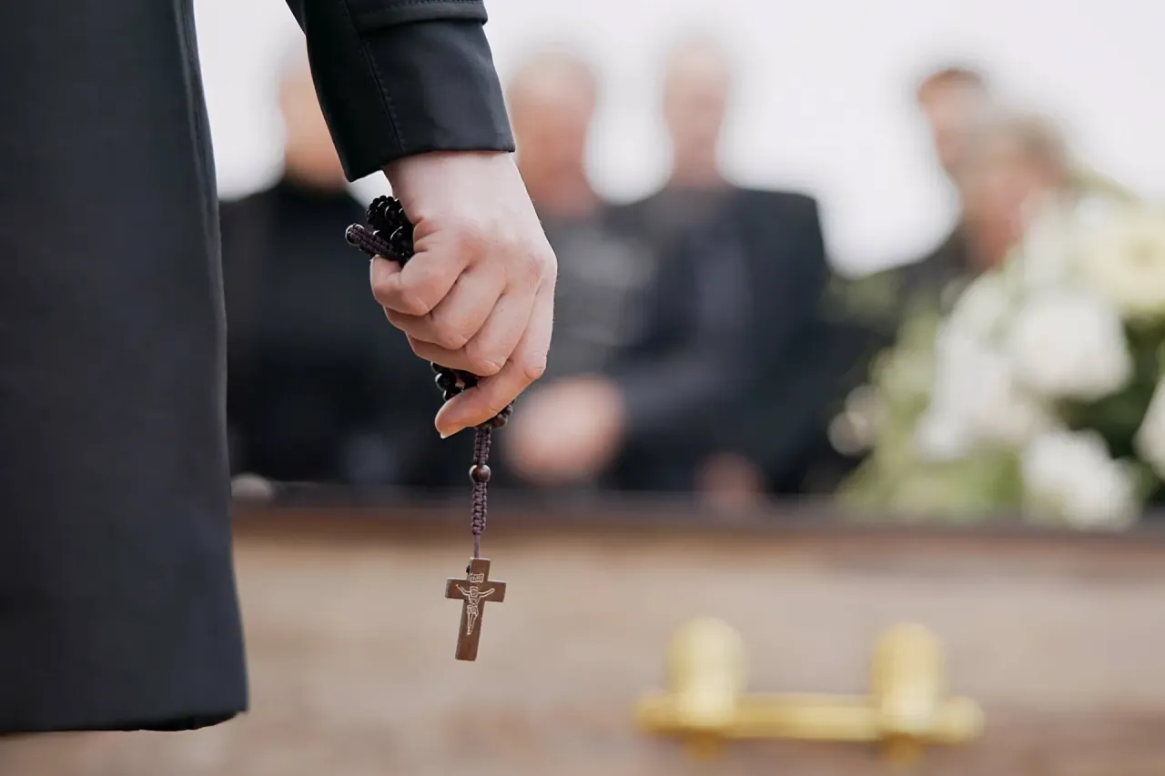 Dłoń trzyma różaniec z krzyżem, symbolizując refleksję nad tym, czy kremacja jest grzechem, podczas pogrzebu.