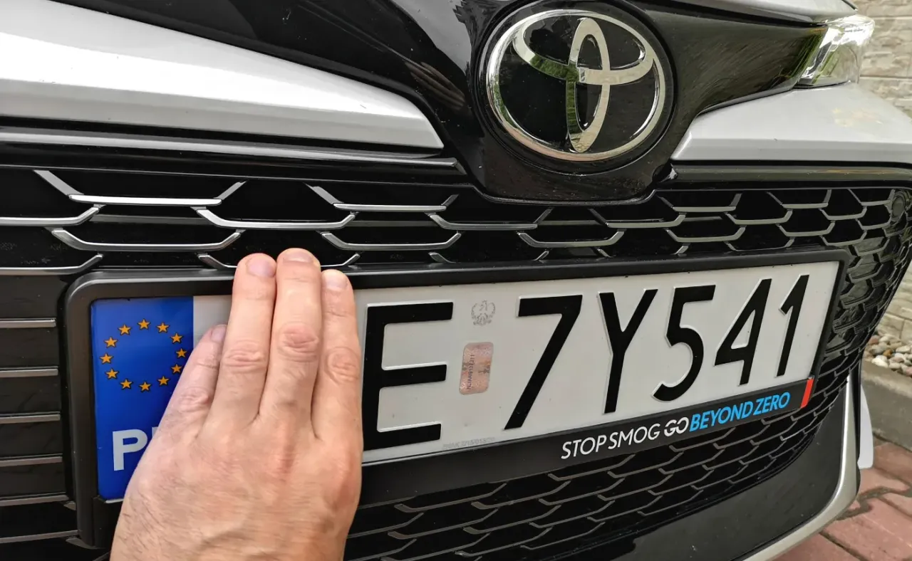 Dłoń zakrywa część tablicy rejestracyjnej z numerem E 7Y541. Czy handlarz musi zarejestrować samochód sprowadzony z zagranicy?