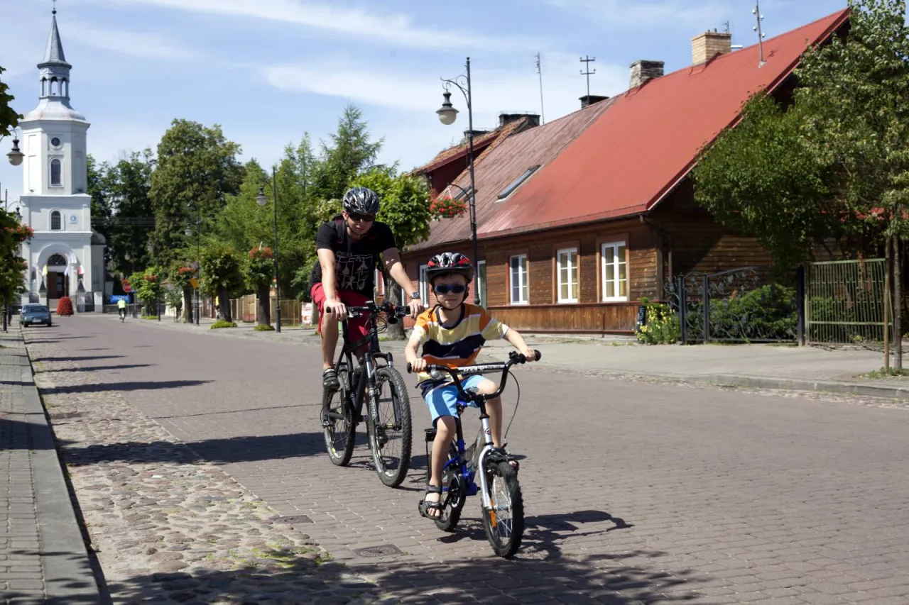 Ojciec i syn na rowerach odkrywają urokliwe trasy rowerowe Białegostoku. Słoneczny dzień sprzyja rodzinnym wycieczkom.