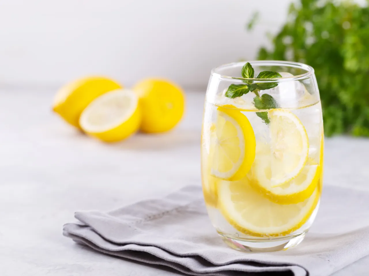 Orzeźwiająca woda z cytryną i miętą, co daje woda z cytryną? Nawodnienie i witamina C. Na stole leżą cytryny i zielona pietruszka.