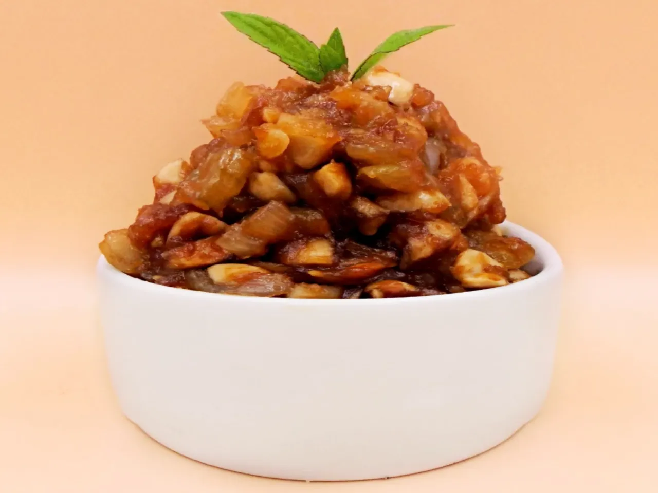 Sos z masła orzechowego i sosu sojowego, z kawałkami orzech&oacute;w i listkami mięty, w białej miseczce.