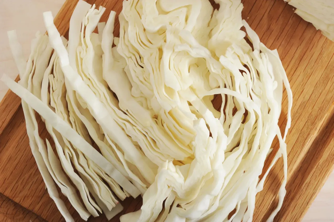 Posiekana biała kapusta na desce. Czy surowa kapusta jest zdrowa? Tak, jest pełna witamin i błonnika.