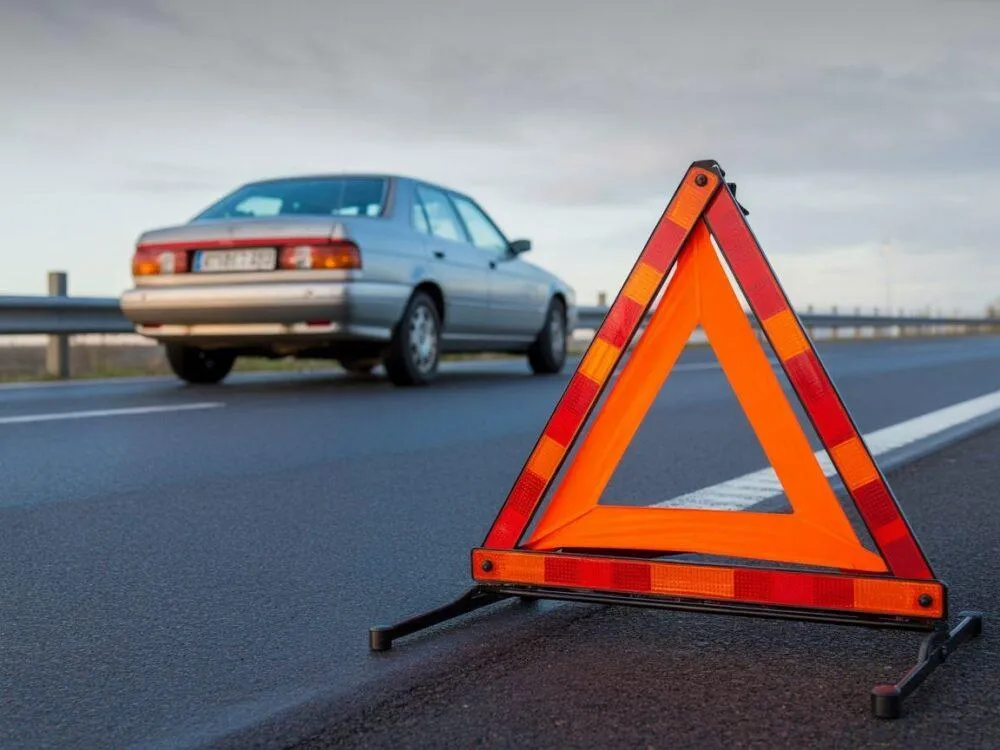 samoch&oacute;d na pasie awaryjnym z tr&oacute;jkątem ostrzegawczym i osobą w kamizelce