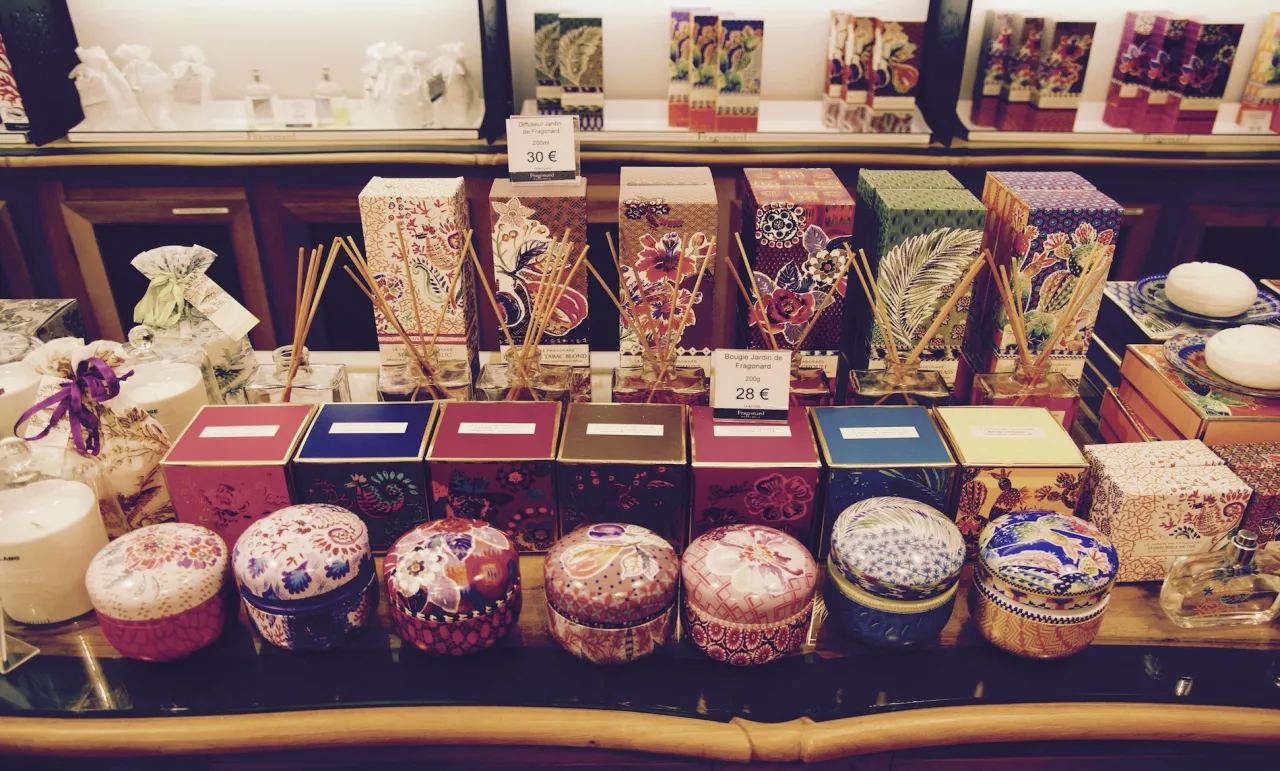 Wystawa w muzeum perfum w Paryżu: kolorowe pudełka, dyfuzory, świece i ozdobne puszki.