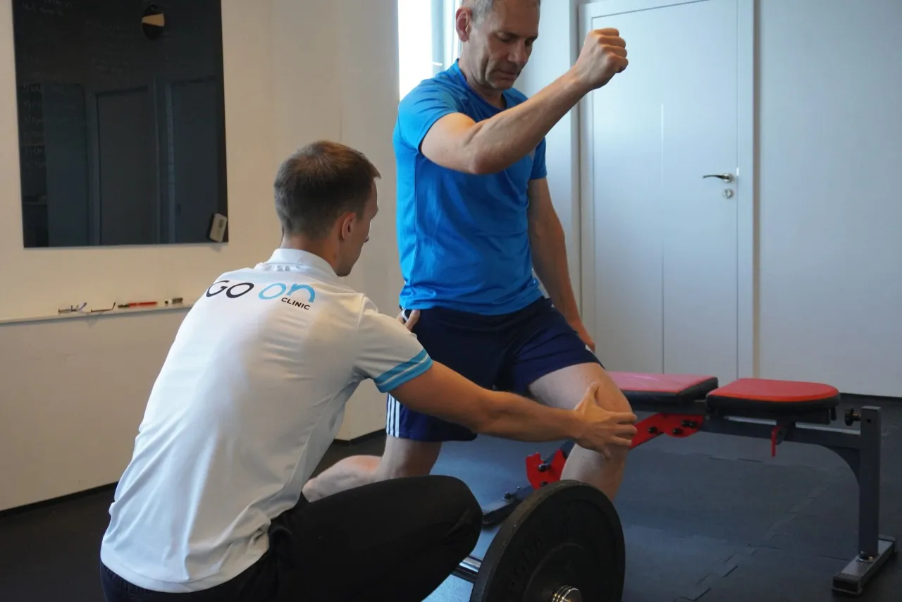 Fizjoterapeuta pomaga pacjentowi w ćwiczeniu, pokazując jak prawidłowo wykonać ruch. To przykład treningu oporowego, co to jest i jak działa.