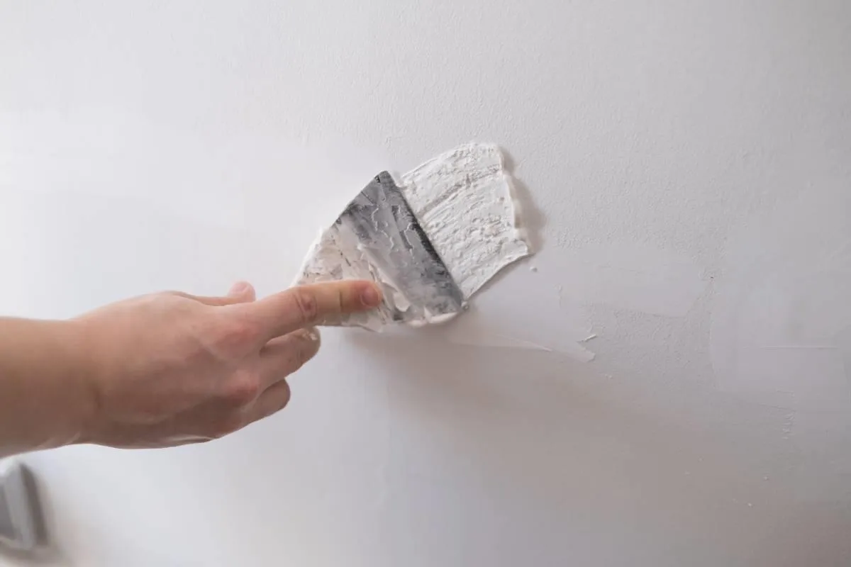 Dłoń zacierająca gips szpachlowy na białej ścianie. Czas, ile schnie gips szpachlowy, zależy od warunk&oacute;w.