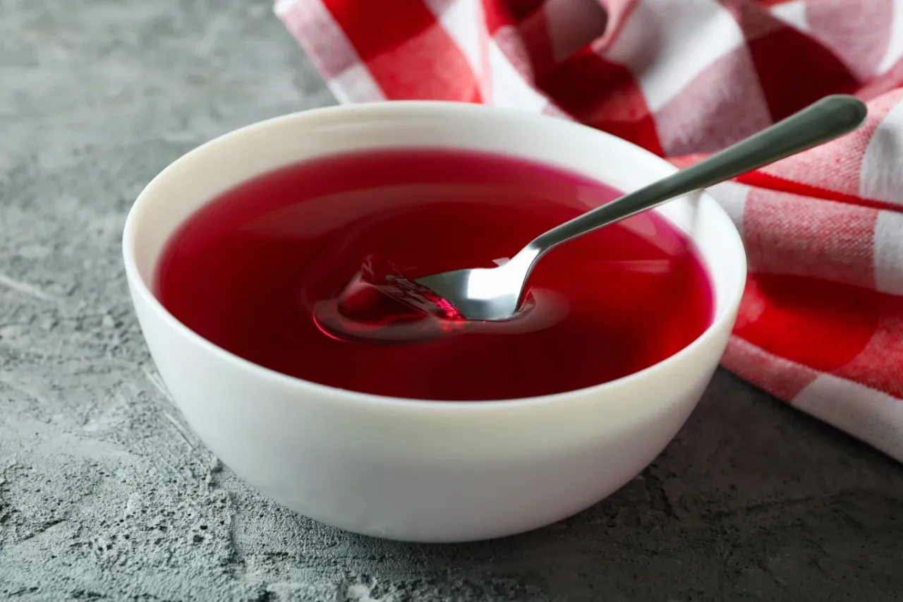 Czerwona galaretka w białej misce, łyżeczka zanurzona w niej. Czy w galaretce jest kolagen? Taka myśl nasuwa się, gdy patrzymy na ten deser.