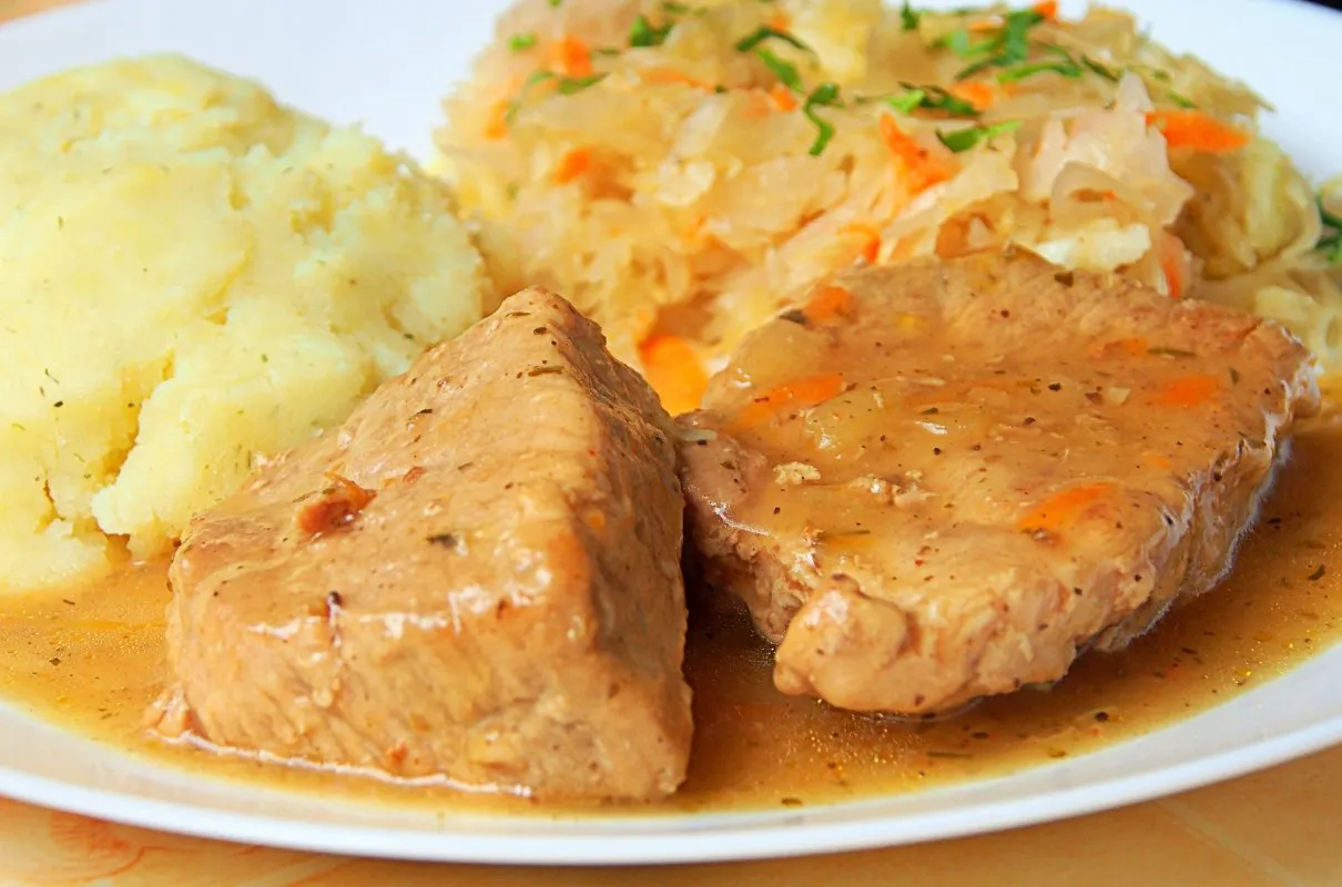 Dwa kawałki szynki wieprzowej w sosie, podane z pur&eacute;e ziemniaczanym i sur&oacute;wką z kiszonej kapusty. Idealny pomysł, co ugotować z szynki wieprzowej.
