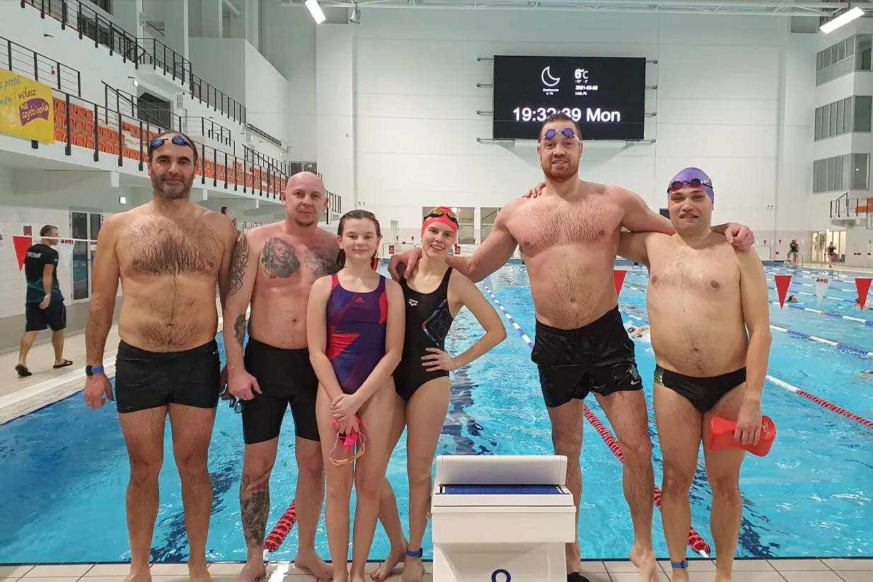 Grupa os&oacute;b w strojach kąpielowych pozuje przy basenie. Może to być dow&oacute;d, że można nauczyć się pływać w jeden dzień!