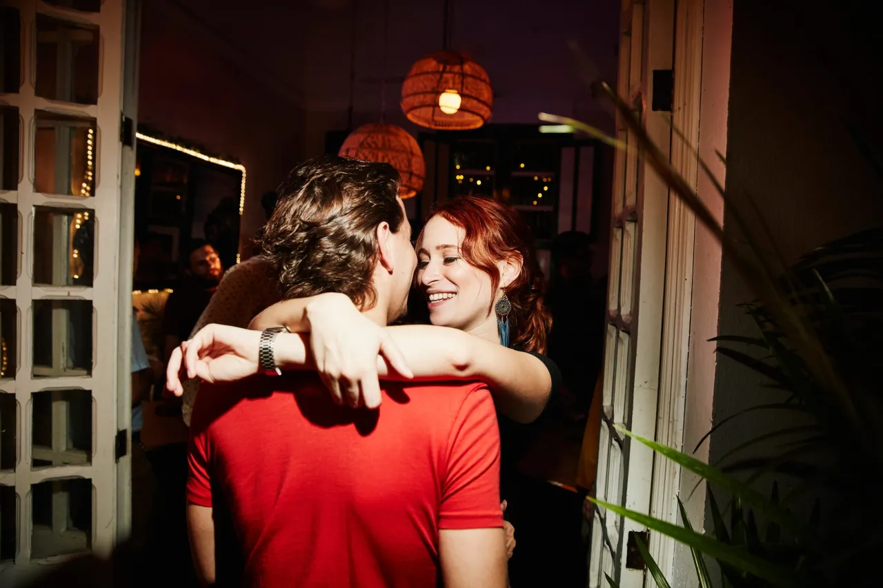 Uśmiechnięta kobieta obejmuje mężczyznę. W tle widać innych ludzi i lampy. To może być scena, jak podrywa facet po 50.