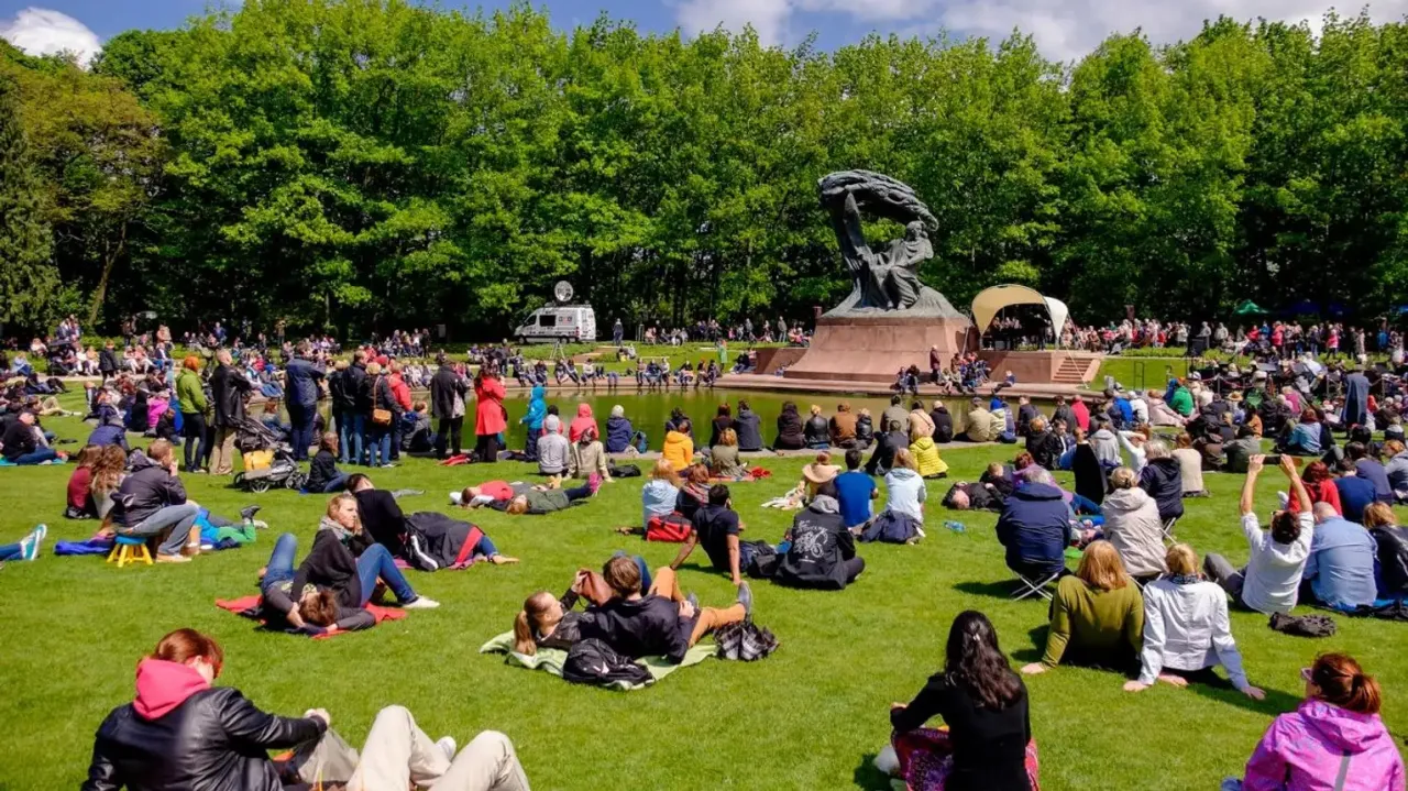 Koncert chopinowski w Łazienkach Kr&oacute;lewskich w Warszawie. Tłumy ludzi siedzą na trawie, słuchając muzyki.