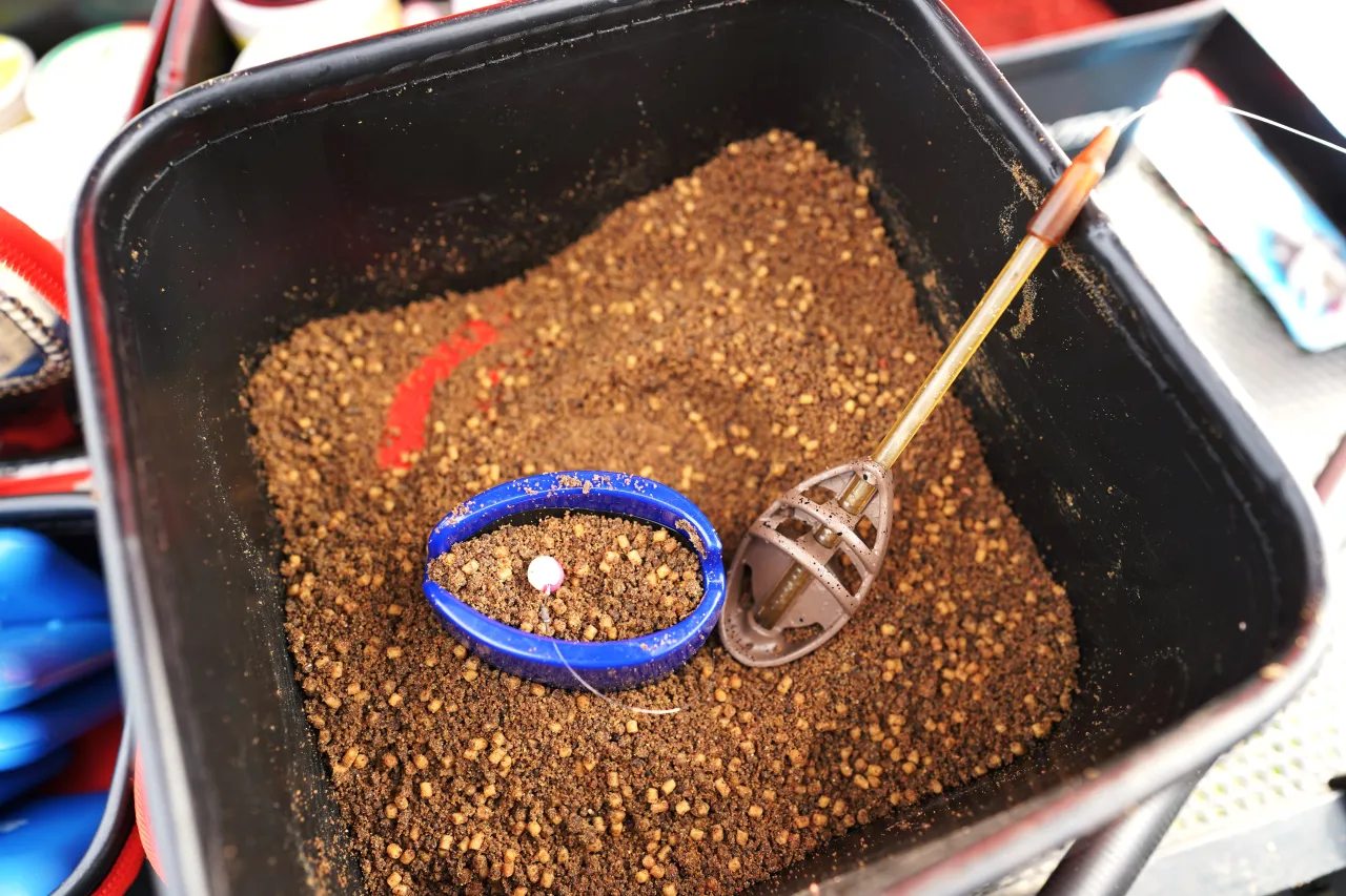 Wiadro z zanętą do metody, niebieska foremka z przynętą i brązowy podajnik. To najlepsza zanęta do metody, która przyciągnie ryby.