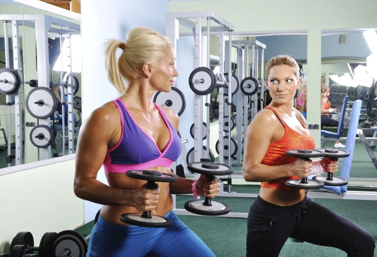 Dwie kobiety ćwiczą z hantlami na siłowni. Idealny obrazek, by pokazać, jak zacząć ćwiczyć na siłowni.