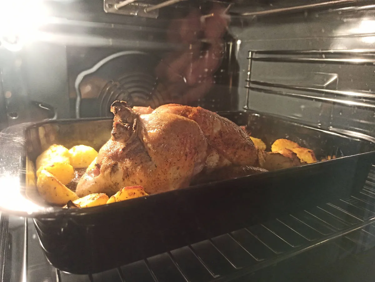 Cały kurczak piecze się w piekarniku z ziemniakami.