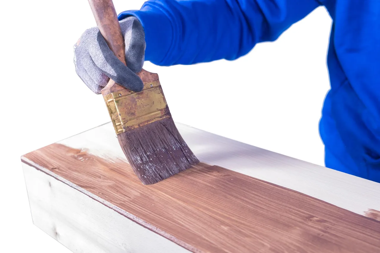 Ręka w rękawicy maluje drewno pędzlem. To pokazuje, czym zabezpieczyć pergole, by służyły latami.