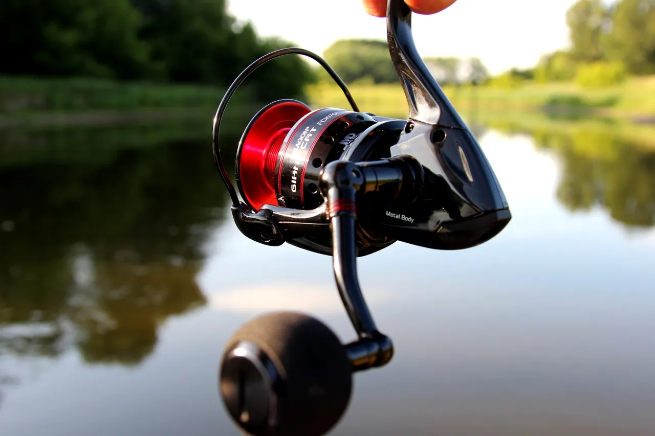 Czarny kołowrotek do spinningu na szczupaka z czerwoną szpulą, gotowy do akcji nad wodą.