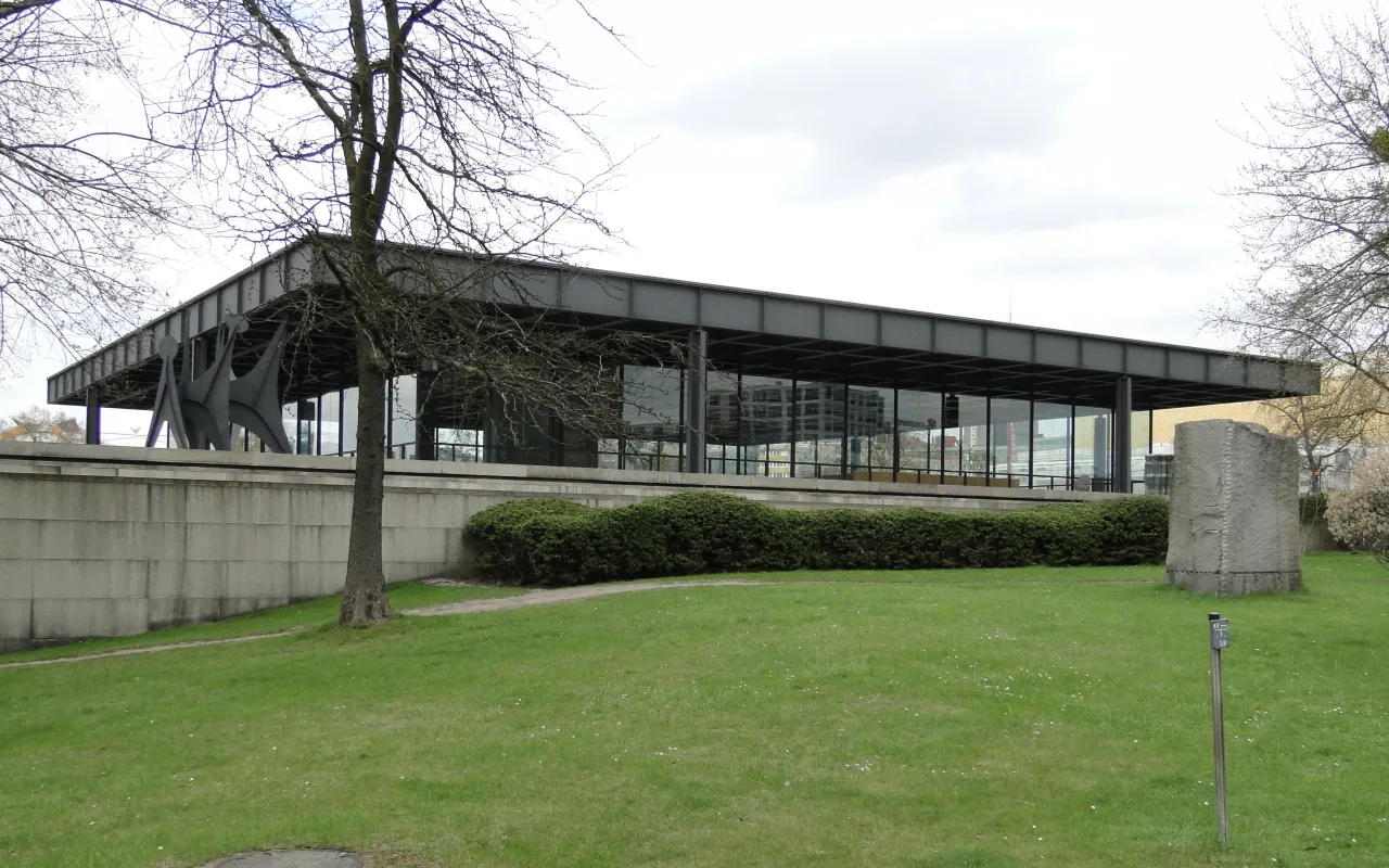 Nowoczesna architektura muzeum sztuki nowoczesnej w Berlinie, z przeszklonymi ścianami i stalową konstrukcją, otoczona zielenią i rzeźbami.