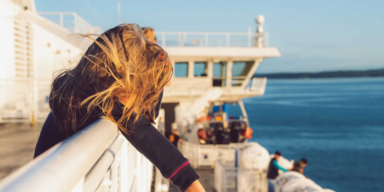 Dziewczynka z rozwianymi włosami opiera się o burtę statku, czując objawy choroby morskiej podczas rejsu na Wyspy Kanaryjskie.