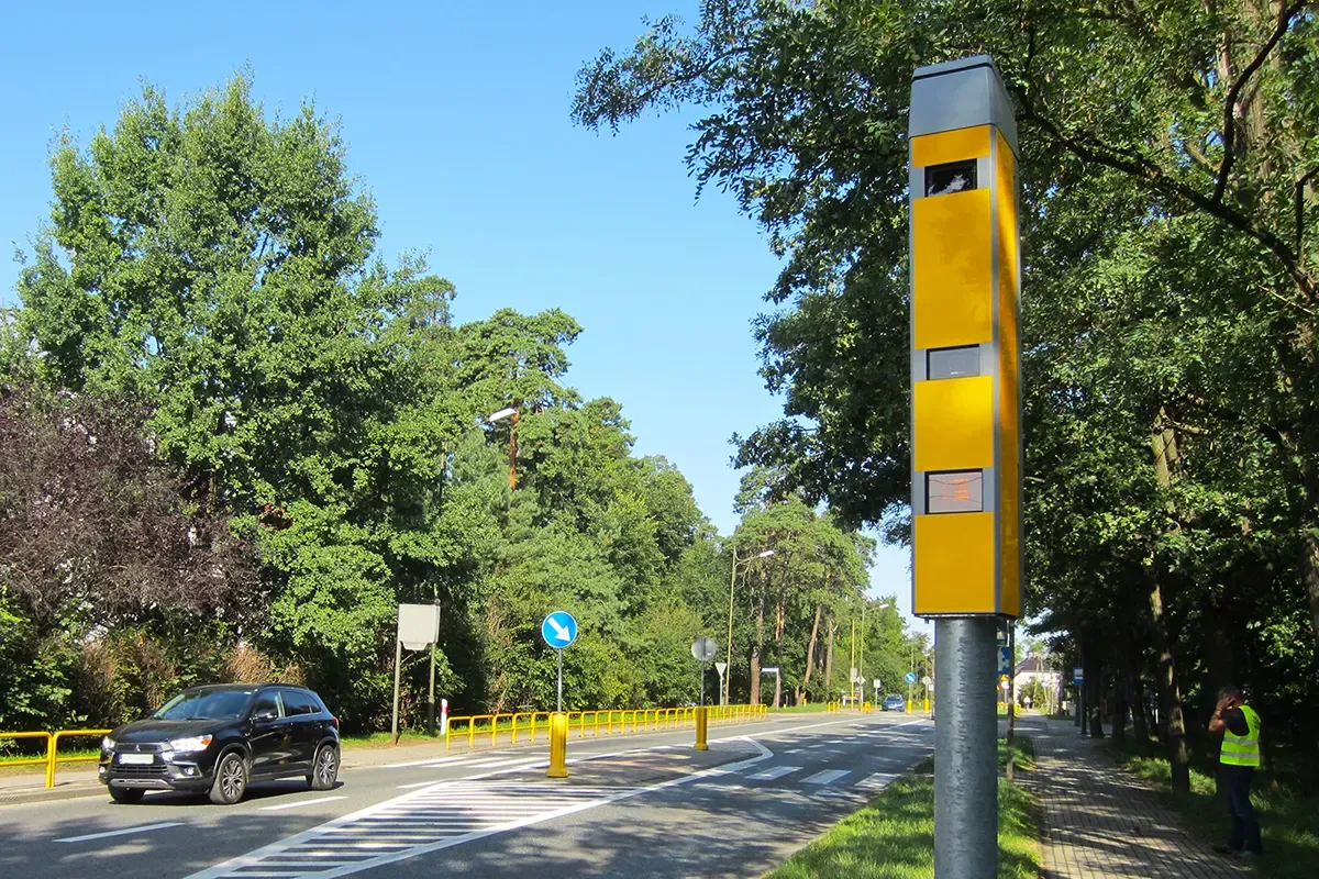 Żółty fotoradar przy drodze, pokazujący, jak działa fotoradar, rejestrując przejeżdżający samochód.