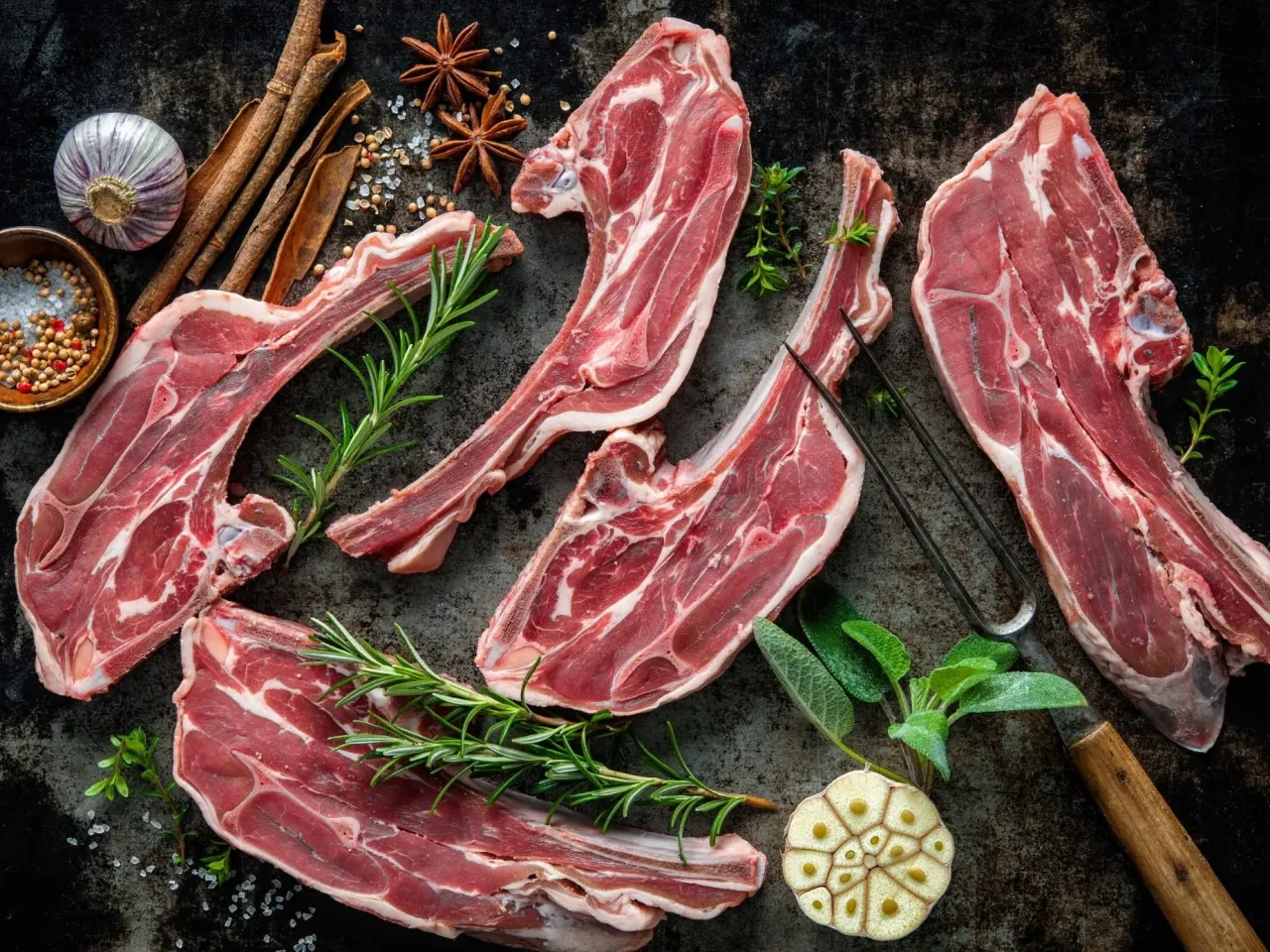 Surowa jagnięcina, co to jest? Kotlety jagnięce z rozmarynem, czosnkiem, cynamonem i gwiazdkami anyżu na ciemnym tle.