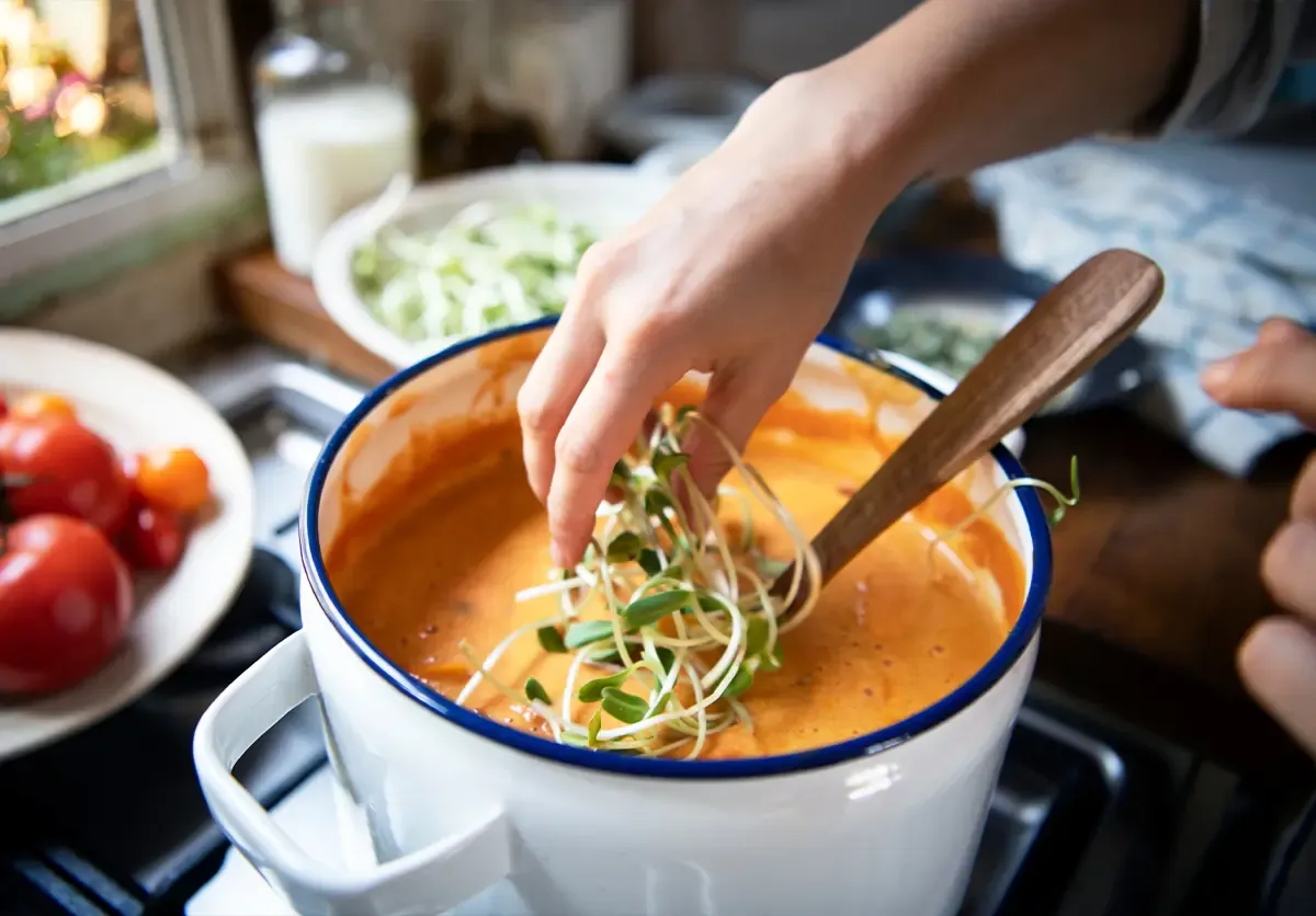 Ręka dodaje kiełki do pomidorowej zupy, by ją nieco złagodzić. Obok pomidory i kapusta.