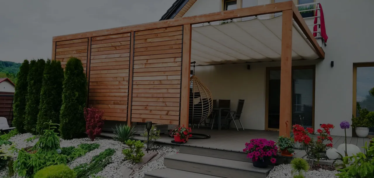 Nowoczesny taras z drewnianą pergolą i zasłonami. Deski tarasowe ułożone są w sposób, który sugeruje, jak klasc deski tarasowe wzdluz czy wszerz, tworząc estetyczną całość.