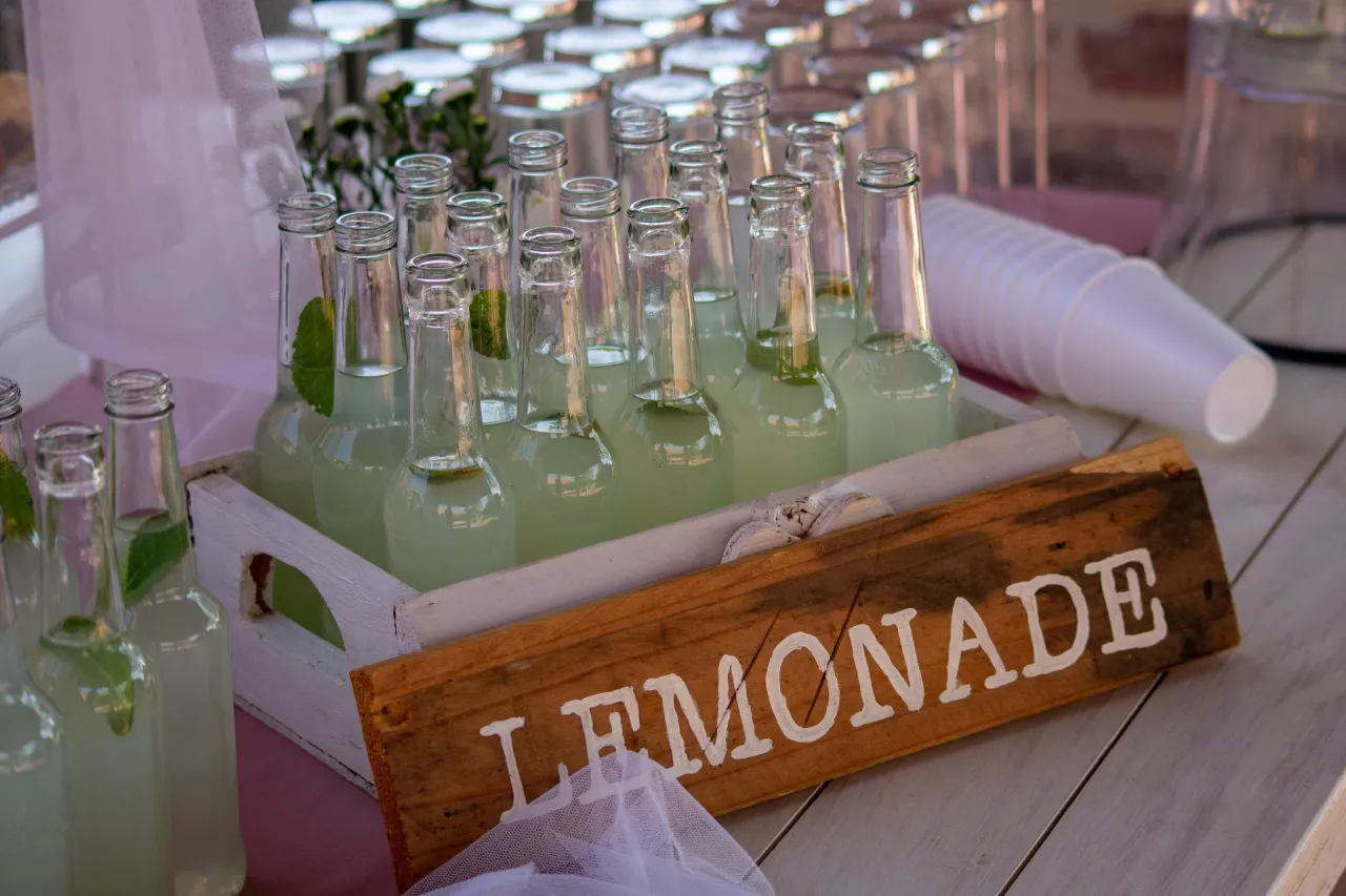 Wiele butelek orzeźwiającej lemoniady czeka w drewnianej skrzynce. To idealny drink bar zamiast barmana na letnie przyjęcie.