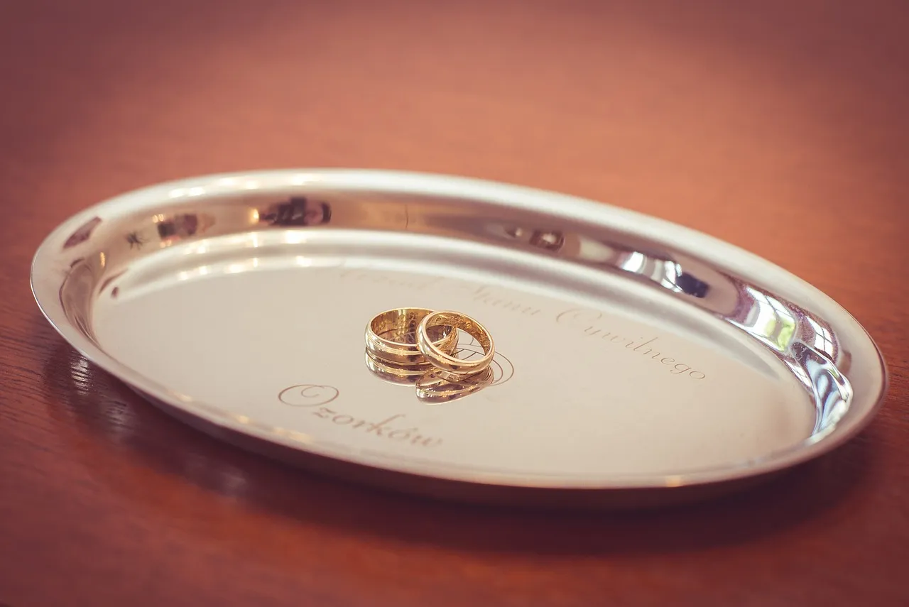 Złote obrączki na srebrnej tacce z grawerem. Jak udokumentować pieniądze z wesela? Ta fotografia może być inspiracją.