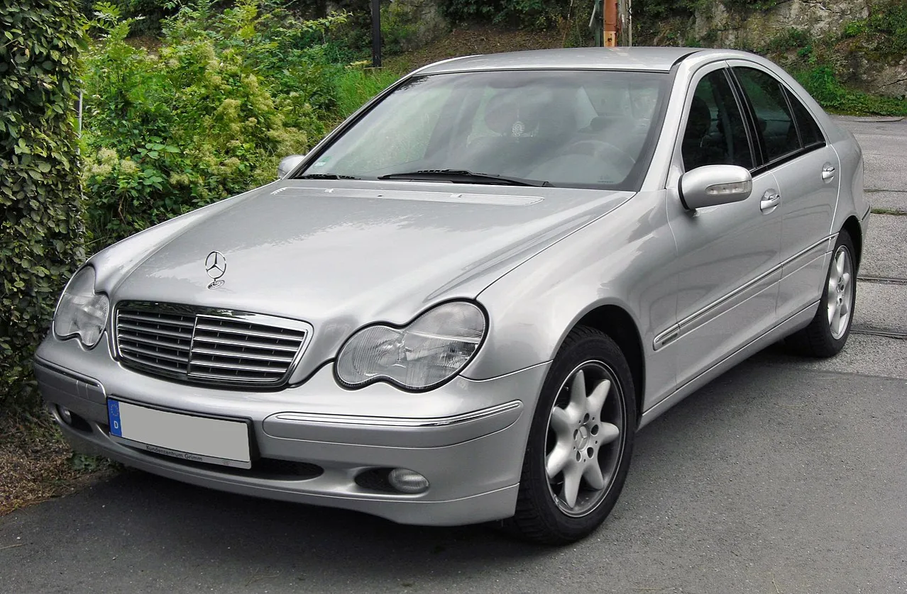 Srebrny Mercedes W203 2.2 CDI zaparkowany przy zielonym żywopłocie.