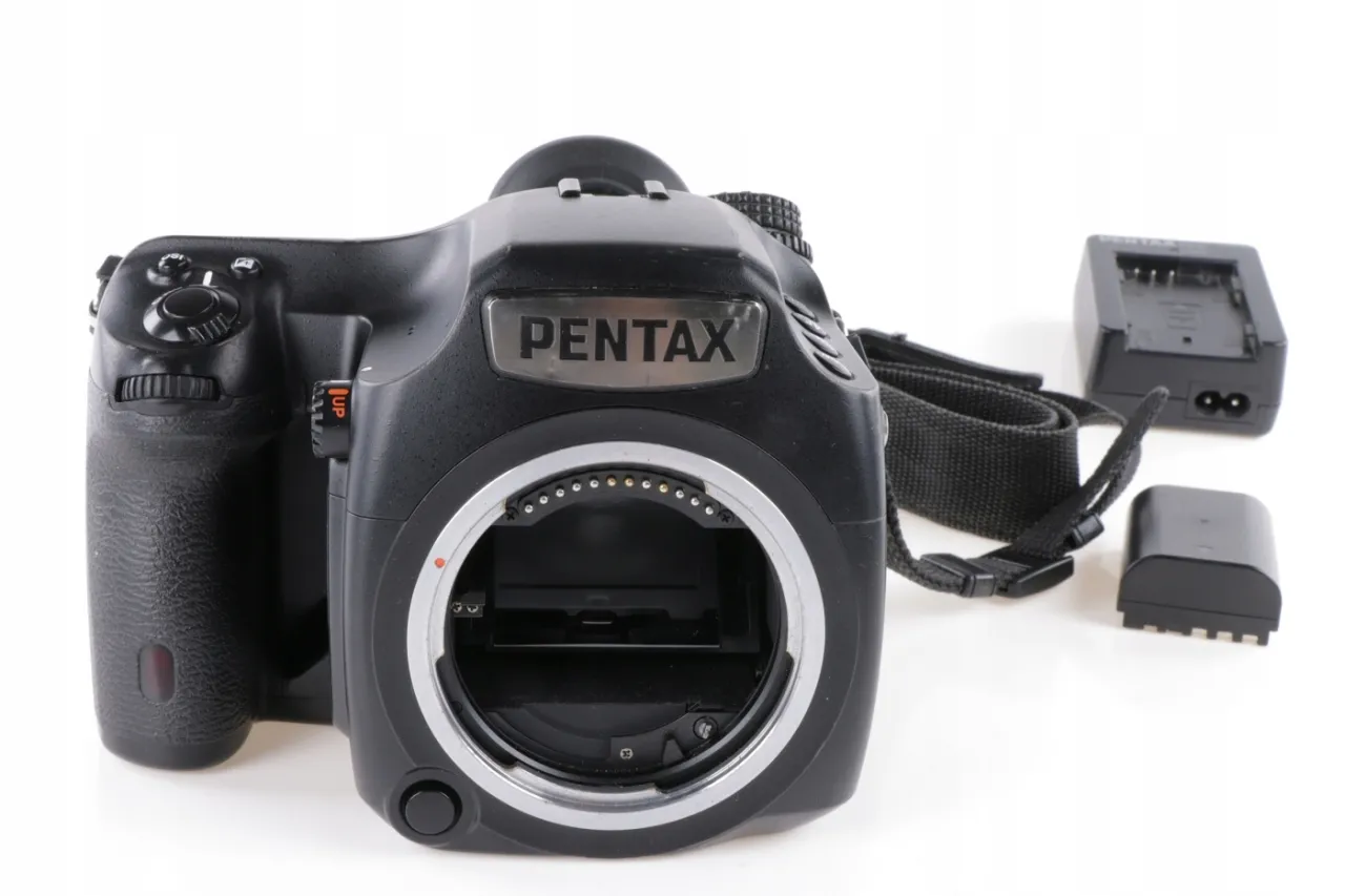 Czarna lustrzanka cyfrowa Pentax z paskiem i akcesoriami, gotowa do aukcji na Allegro.