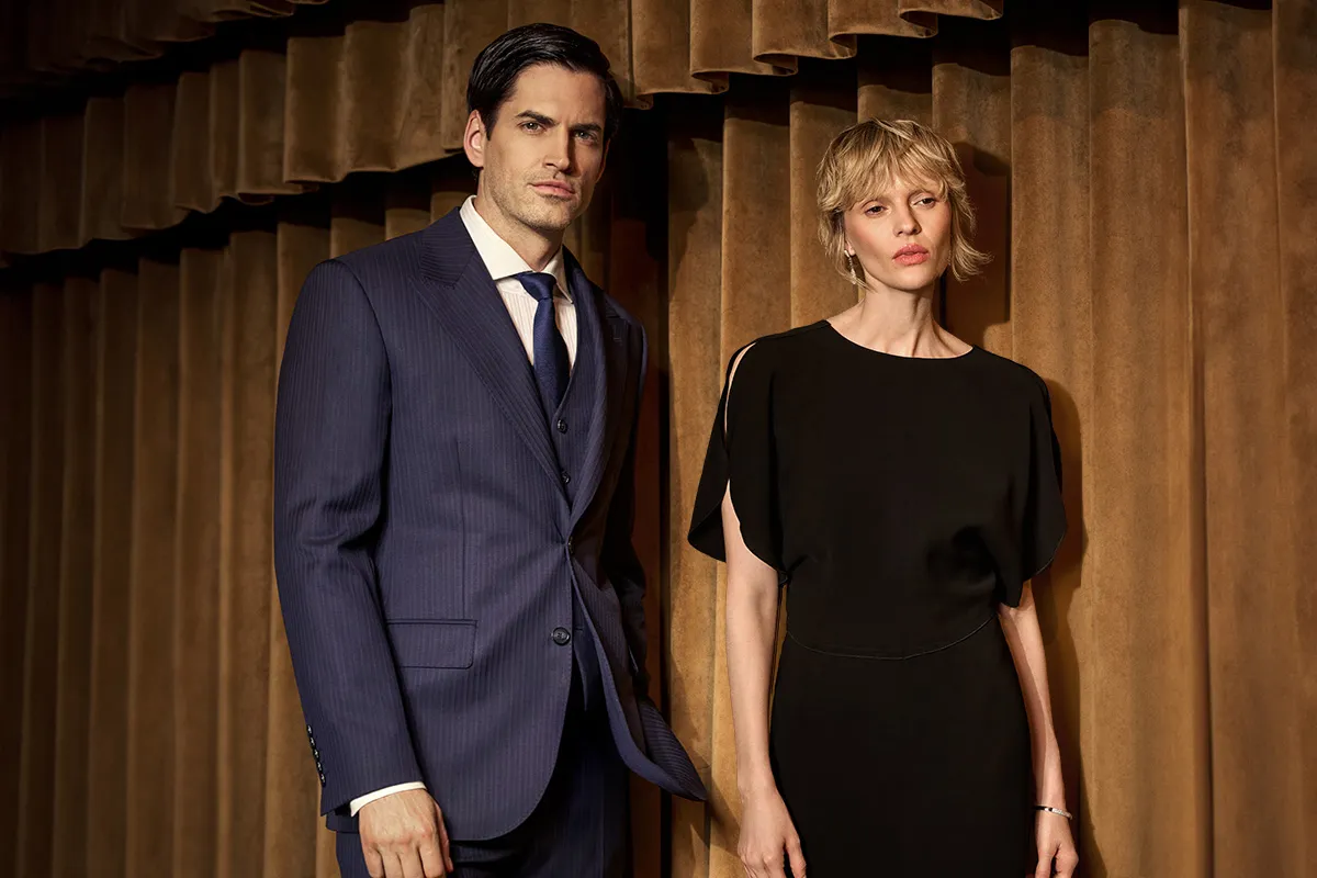 Mężczyzna w granatowym prążkowanym garniturze i kobieta w czarnej sukience. Ukazują różnicę między stylem old money a klasyczną elegancją w modzie wizytowej.