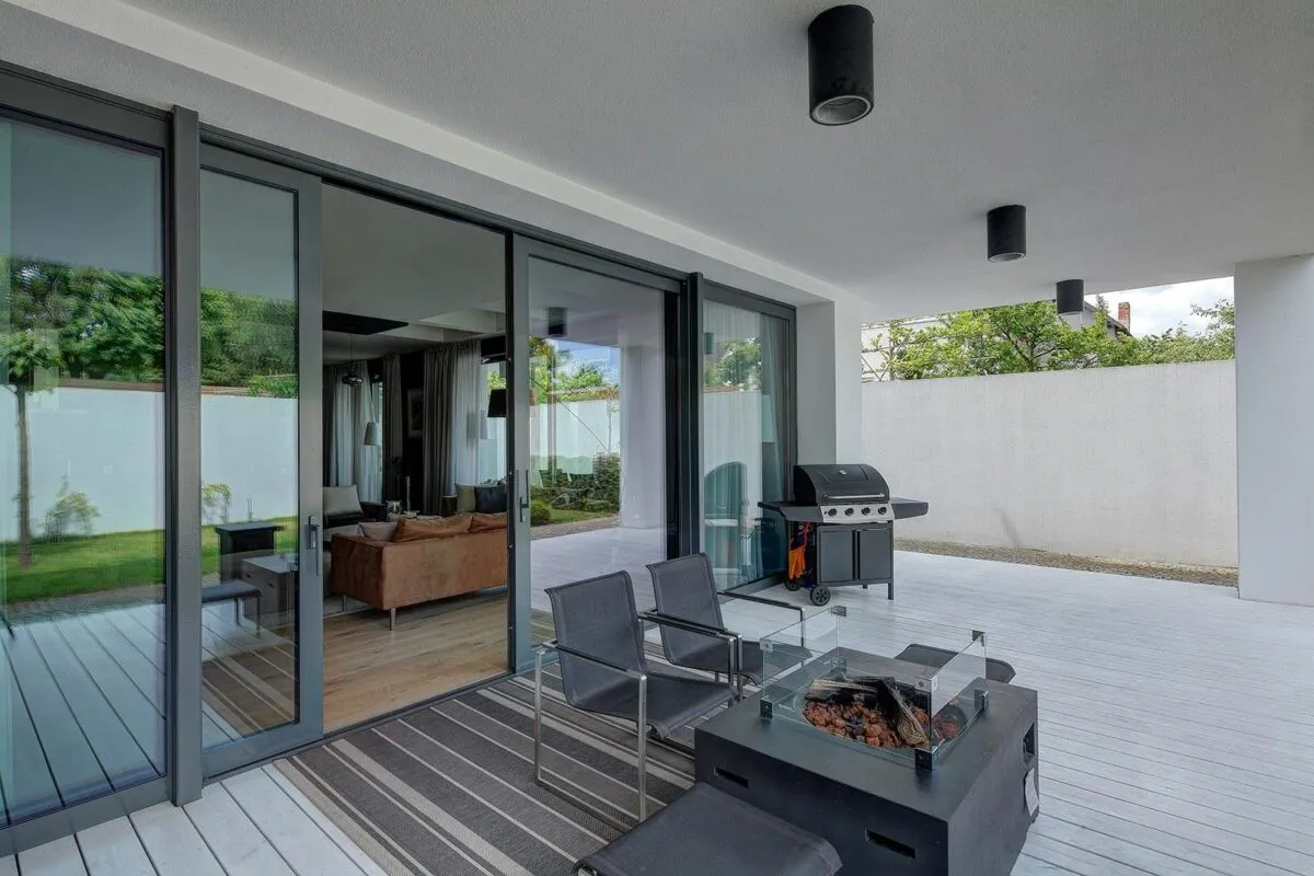 Nowoczesne okna antracytowe z widokiem na salon i taras z grillem.