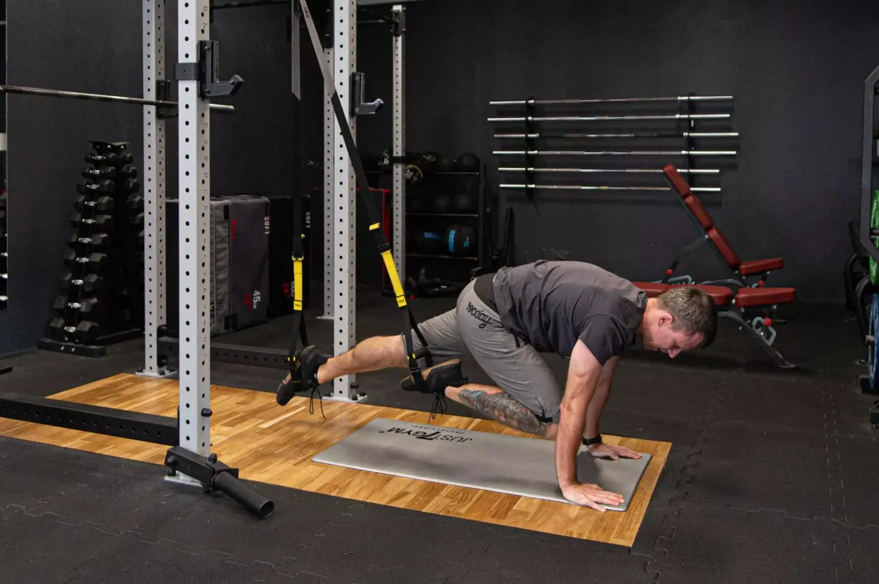 Mężczyzna wykonuje ćwiczenia na TRX, przyciągając kolana do klatki piersiowej w pozycji deski.