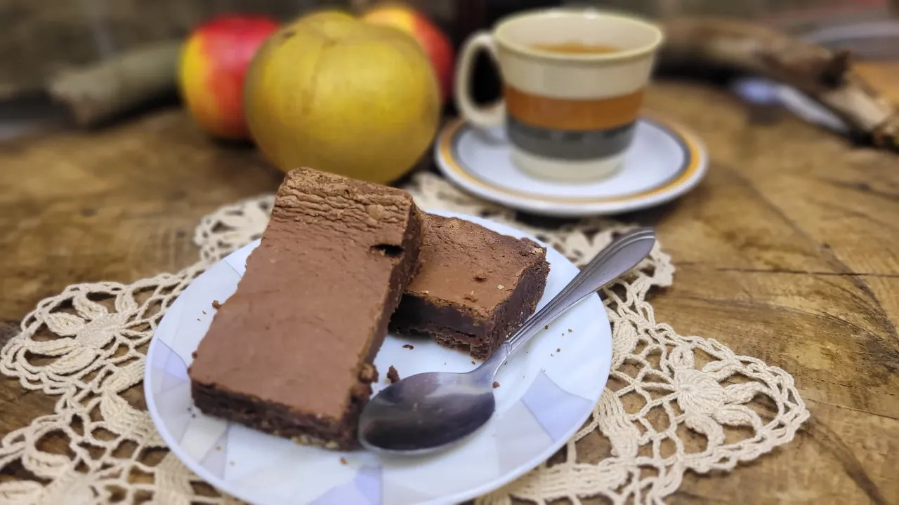 Dwa kawałki brownie na talerzyku z łyżeczką, obok jabłka i filiżanka kawy. Idealny przepis na brownie.