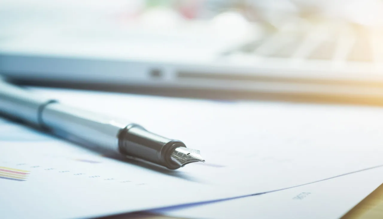 Pióro wieczne na dokumentach, obok laptopa. Czy odpowiedź na pozew doręcza się pełnomocnikowi?