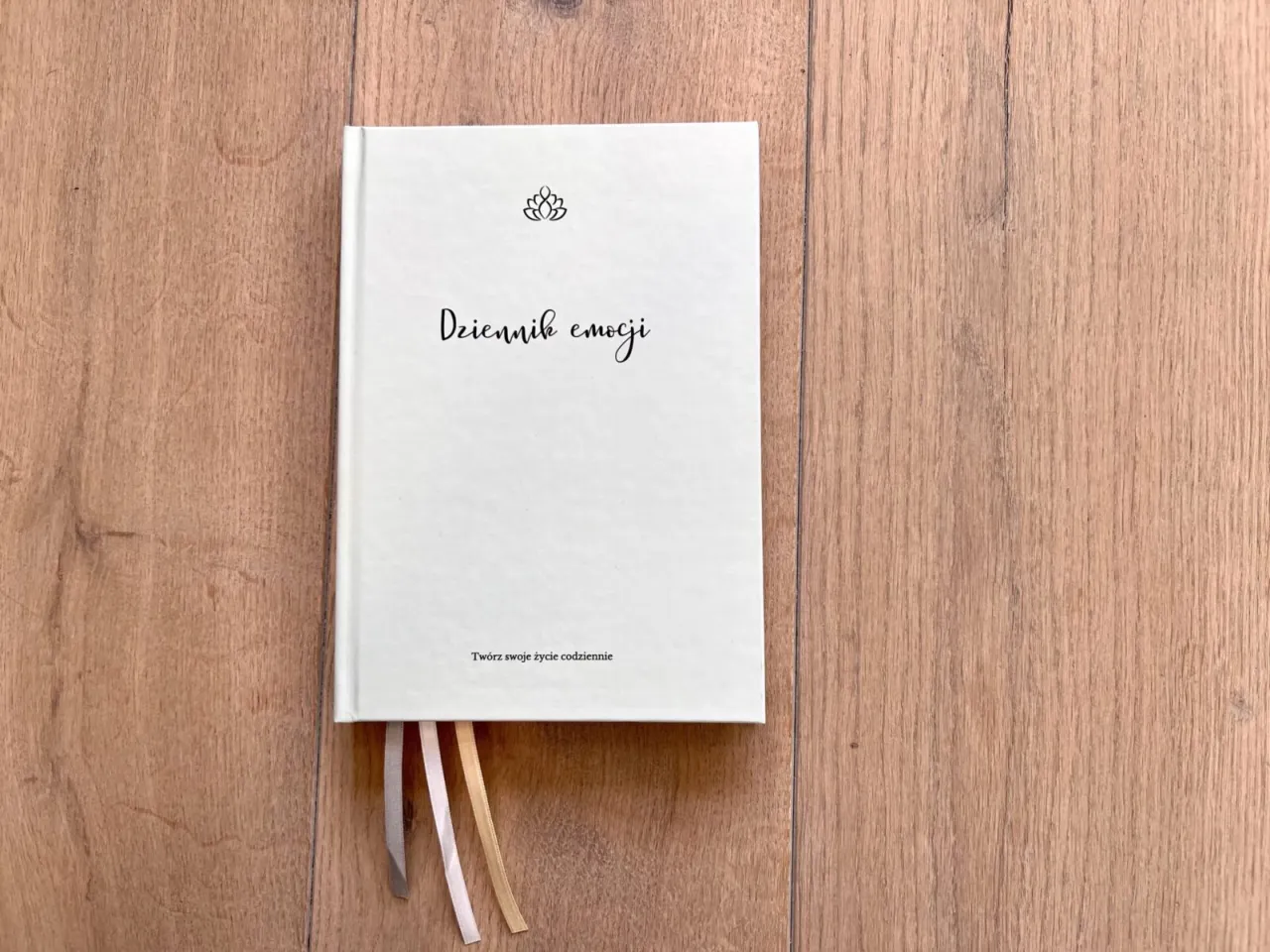 Biały dziennik emocji z subtelnym symbolem lotosu i napisem 