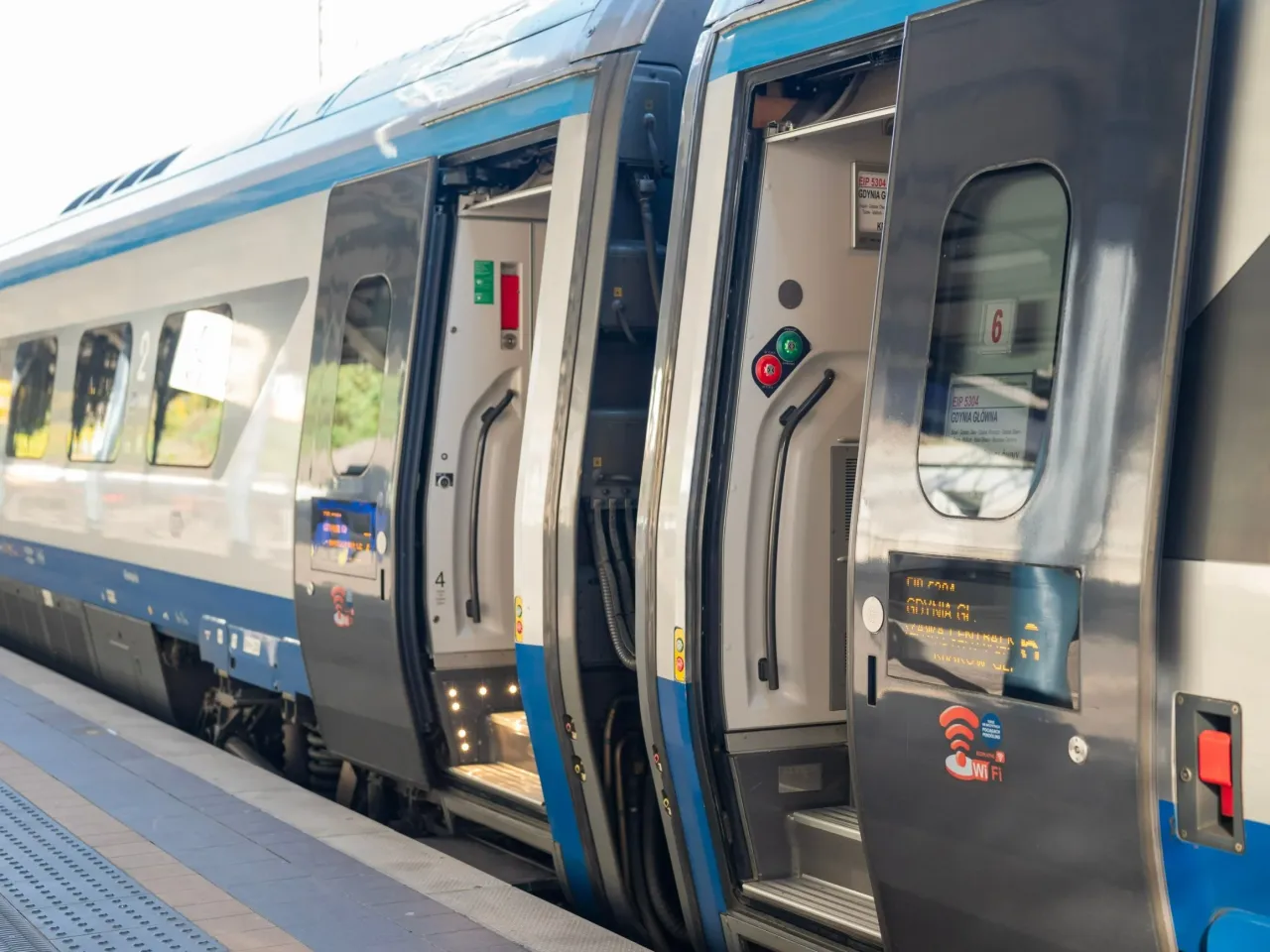 Pociąg TLK z otwartymi drzwiami na peronie. Zastanawiasz się, ile kosztuje bilet TLK? Sprawdź ceny i podr&oacute;żuj!