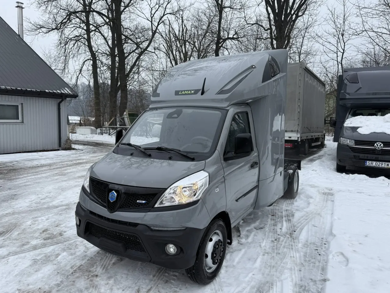 Szary bus LAMAX gotowy na międzynarod&oacute;wkę, zaparkowany na zaśnieżonej drodze obok innego vana.