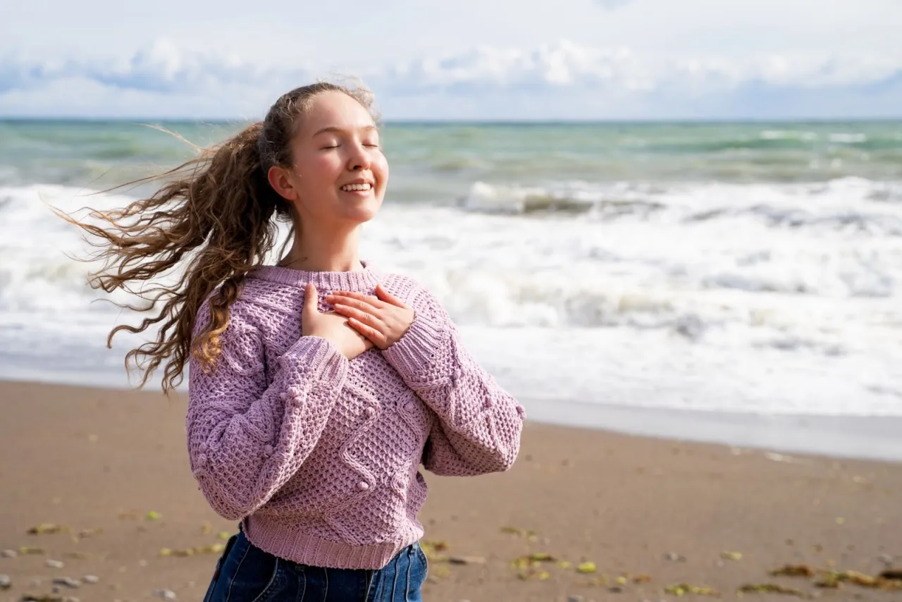 Dziewczyna z rękami na sercu cieszy się morską bryzą. Czy nad każdym morzem jest jod? To pytanie zadaje sobie, wdychając świeże powietrze.