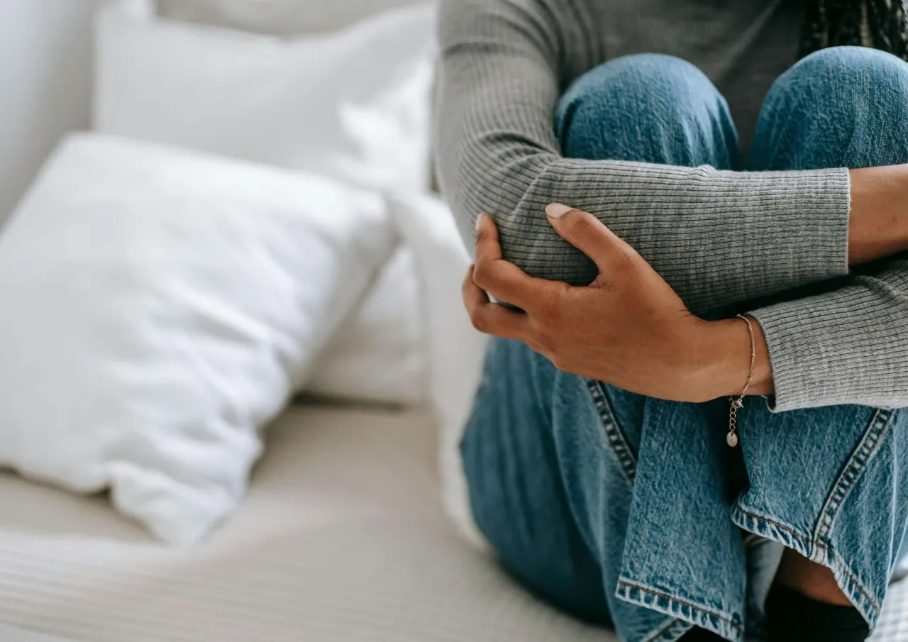 Osoba w jeansach i szarym swetrze przytula kolana. Obraz symbolizuje depresję u nastolatków, jak postępować, szukając wsparcia i nadziei.