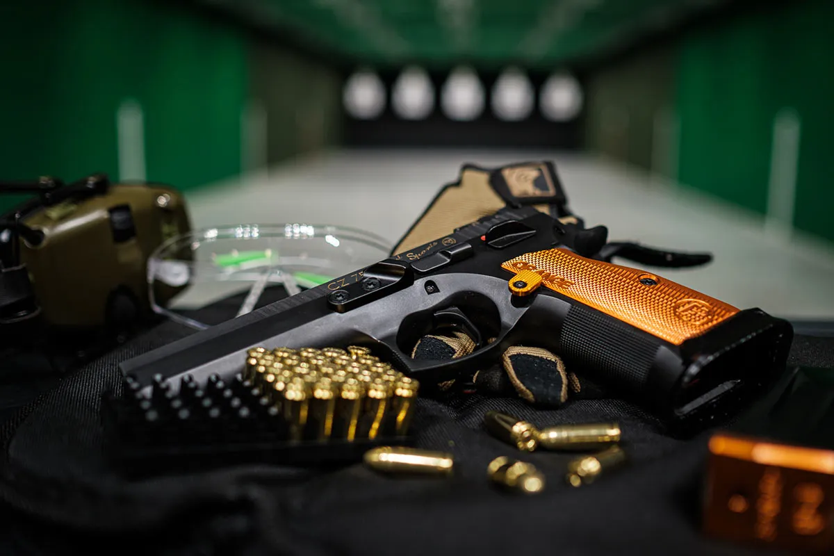 Pistolet CZ 75 SP-01 Shadow z pomarańczową okładziną, amunicją i ochronnikami słuchu na strzelnicy. Czy myśliwy może mieć broń krótką?