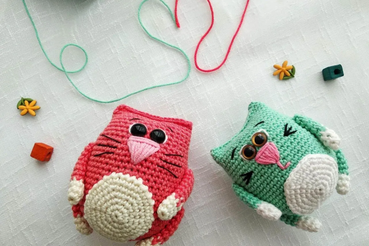 Dwa urocze pluszaki szydełkowane, r&oacute;żowy i zielony kotek, leżą obok siebie.