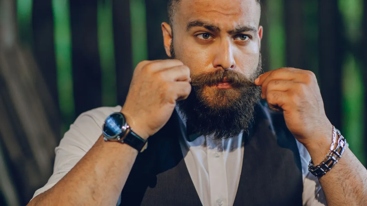 Mężczyzna z brodą i wąsami poprawia swój zarost, pokazując, jak dbać o niego na co dzień.
