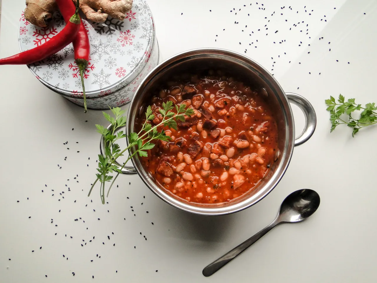 Gorąca fasolka po bretońsku czy pikantne chilli con carne? Aromatyczne danie w garnku, ozdobione natką pietruszki, obok papryczek chili i imbiru.