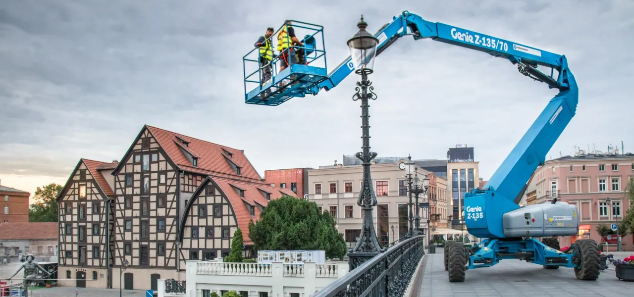 Pracownicy na zwyżce Genie Z-135 naprawiają latarnię. Warto wiedzieć, ile kosztuje godzina pracy zwyżki, by zaplanować takie prace.
