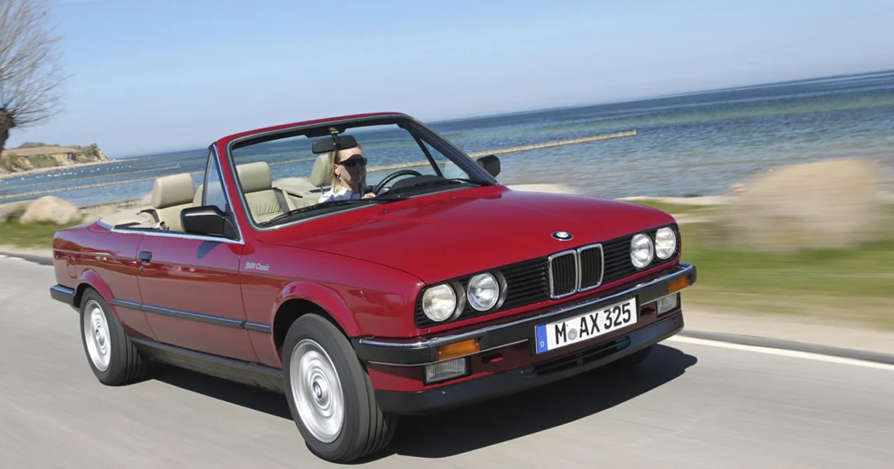 Czerwone bmw e30 cabrio z kobietą za kierownicą jedzie przy morzu.