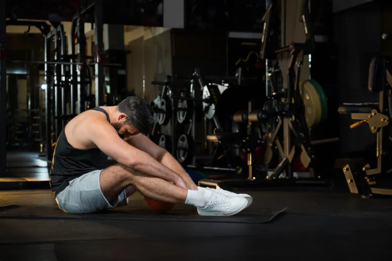 zmęczony sportowiec na siłowni, objawy przetrenowania