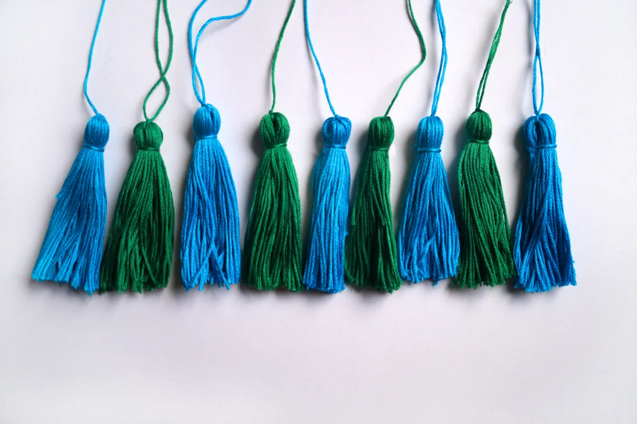 Jak zrobić frędzle? Kilka niebieskich i zielonych frędzli z nici, gotowych do ozdobienia projektu.